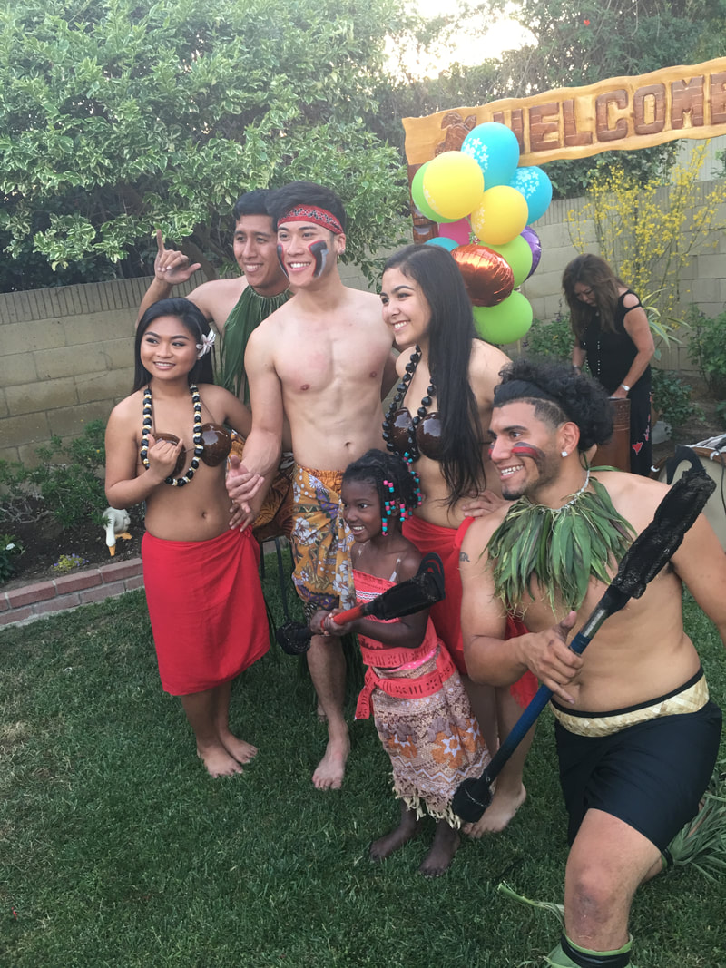 Group in Hawaiian costumes with grass skirts and leis at a backyard luau